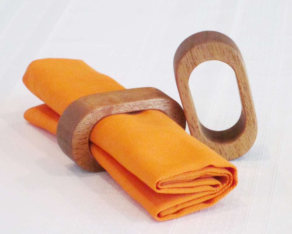Two oval wood napkin rings holding an orange cloth serviette